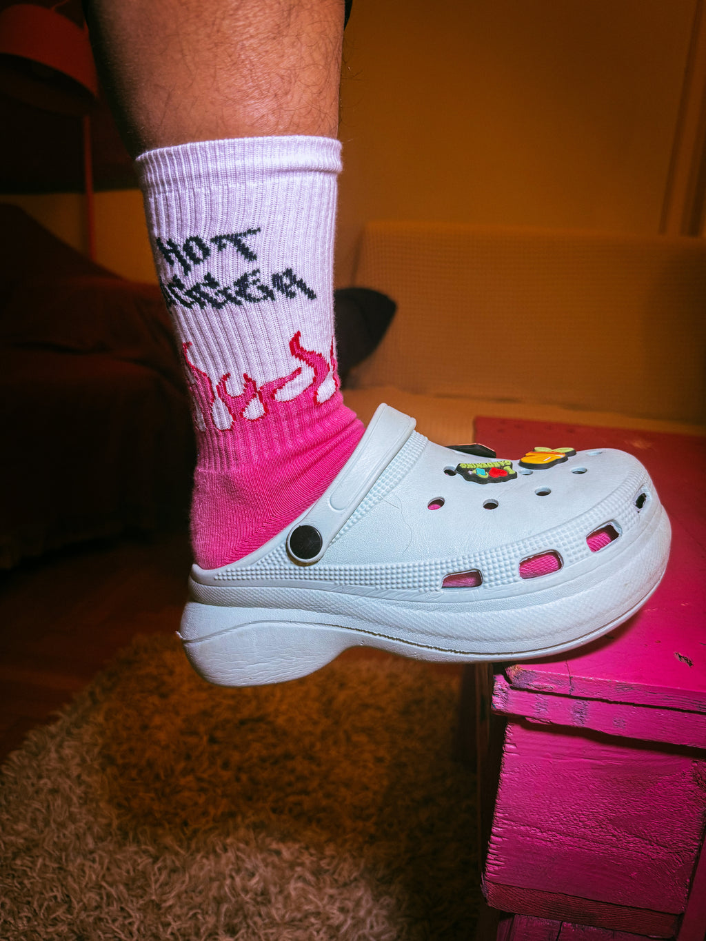 White clog shoe with colorful decorations worn on a foot wearing a pink and white sock.